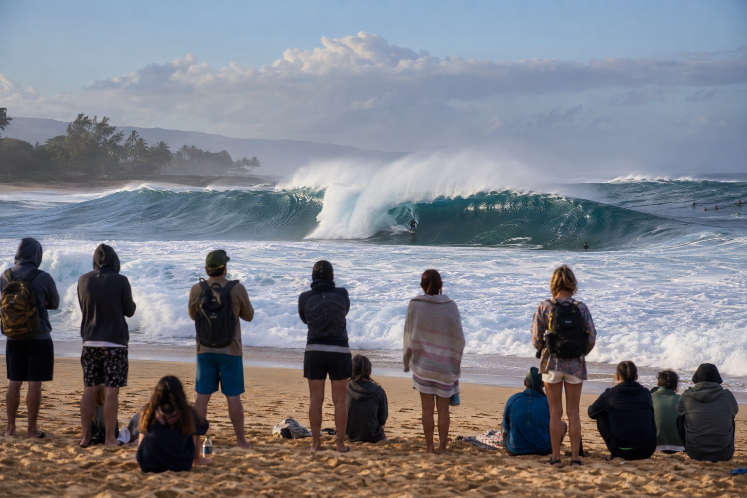 Large winter waves breaking off a North Shore Oahu beach with spectators watching from the sand