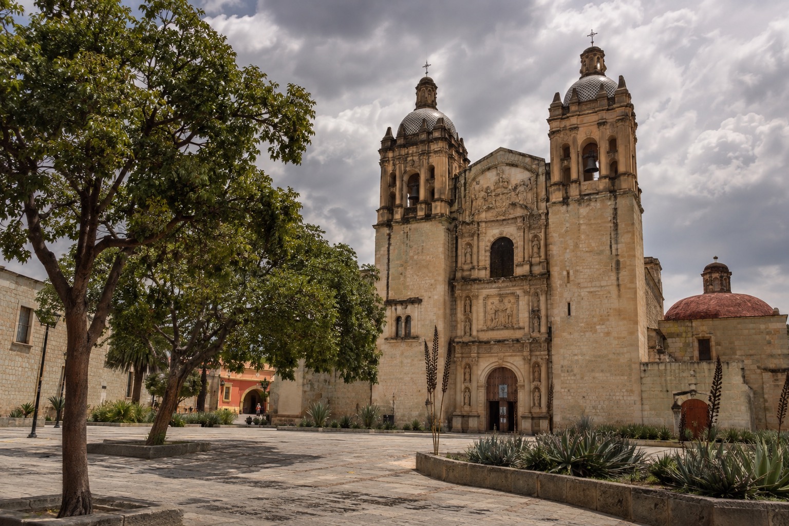 Cathedral facade and laurel trees on a city square in Oaxaca under a cloudy sky