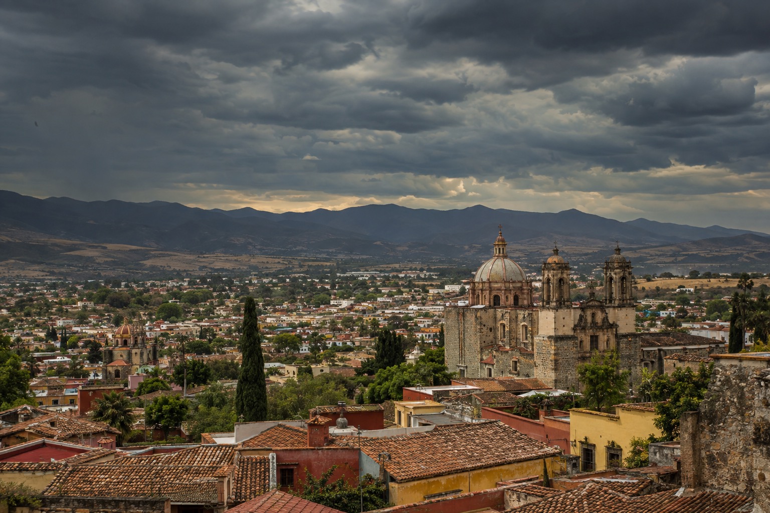 Storm clouds over a valley of low hills and tiled rooftops