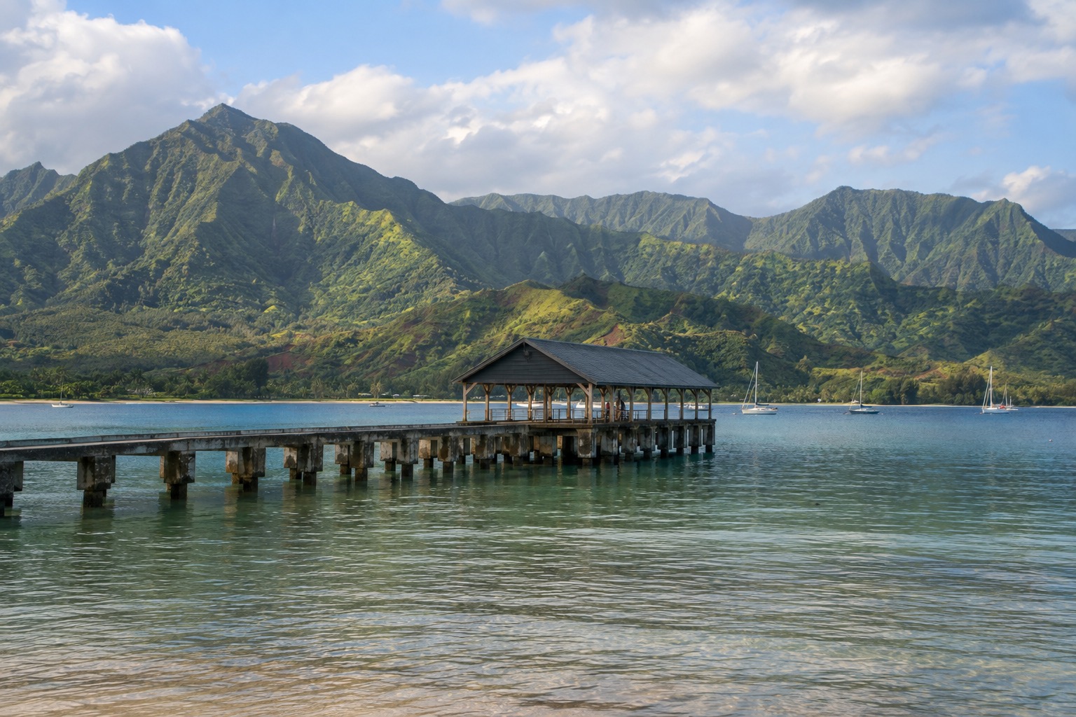 A pier extending into calm water at Hanalei Bay with green mountains behind