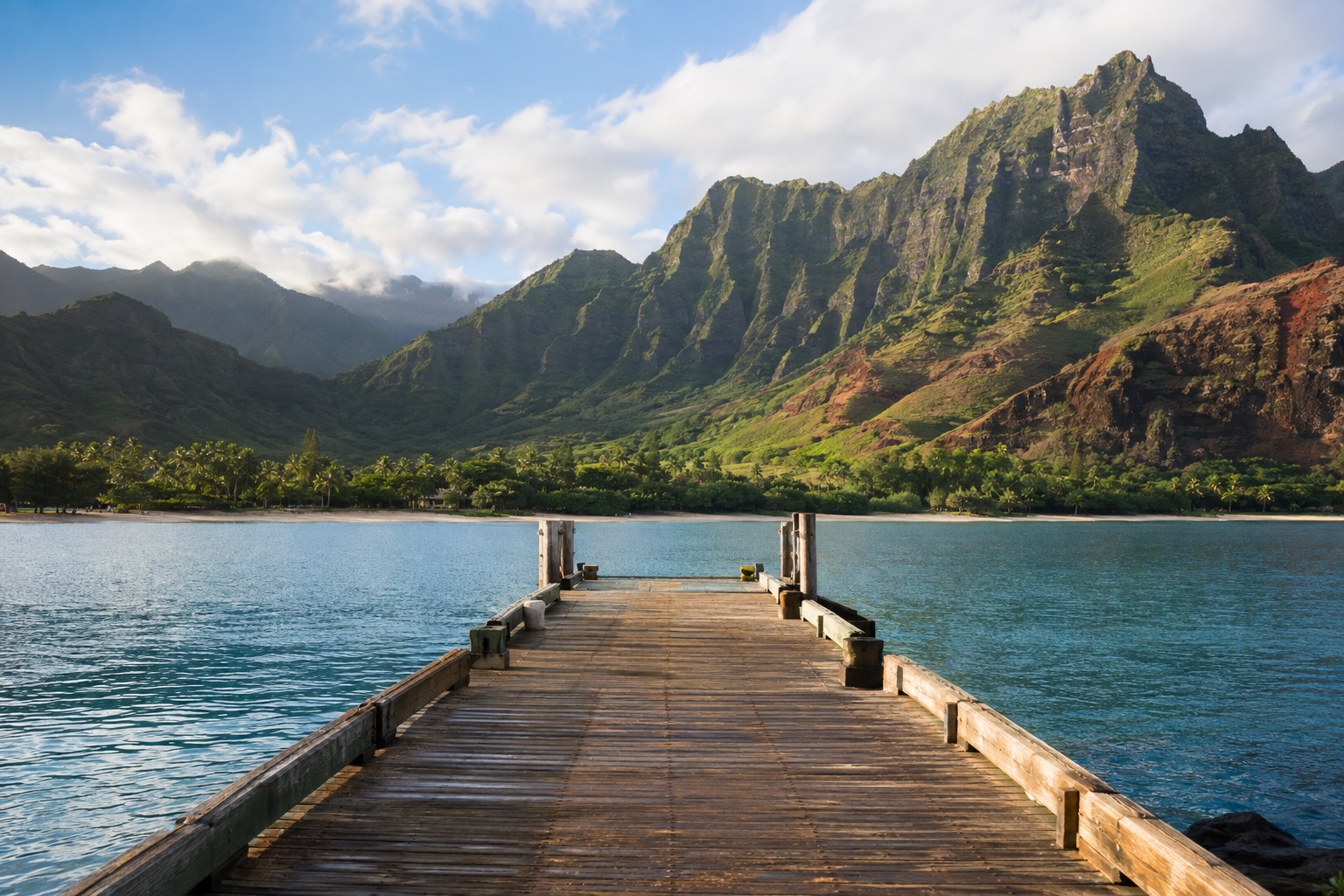 A wooden fishing pier extending into calm water with green mountains in the background
