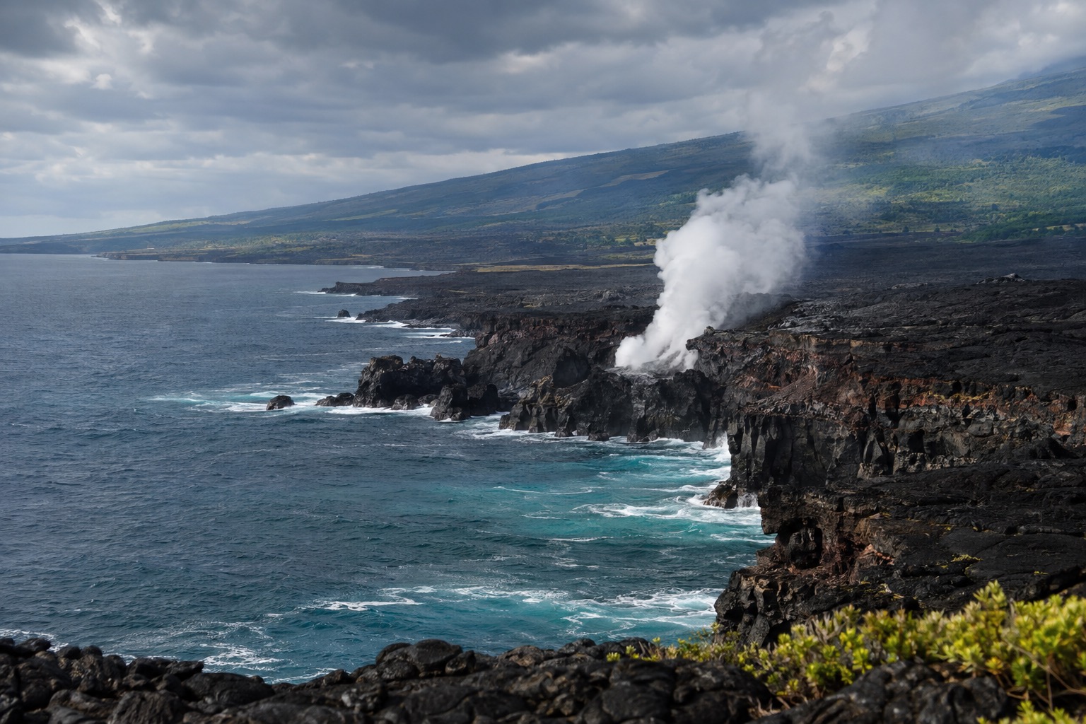 Steam rising from a volcanic vent at Hawaii Volcanoes National Park under an overcast sky