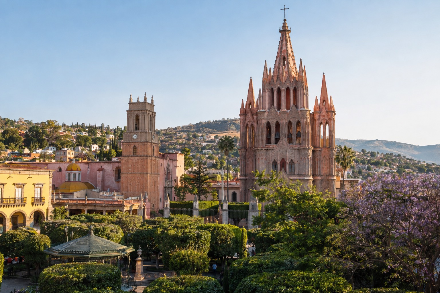 Pink neo-Gothic church towers rising above a tree-lined colonial plaza under a clear sky