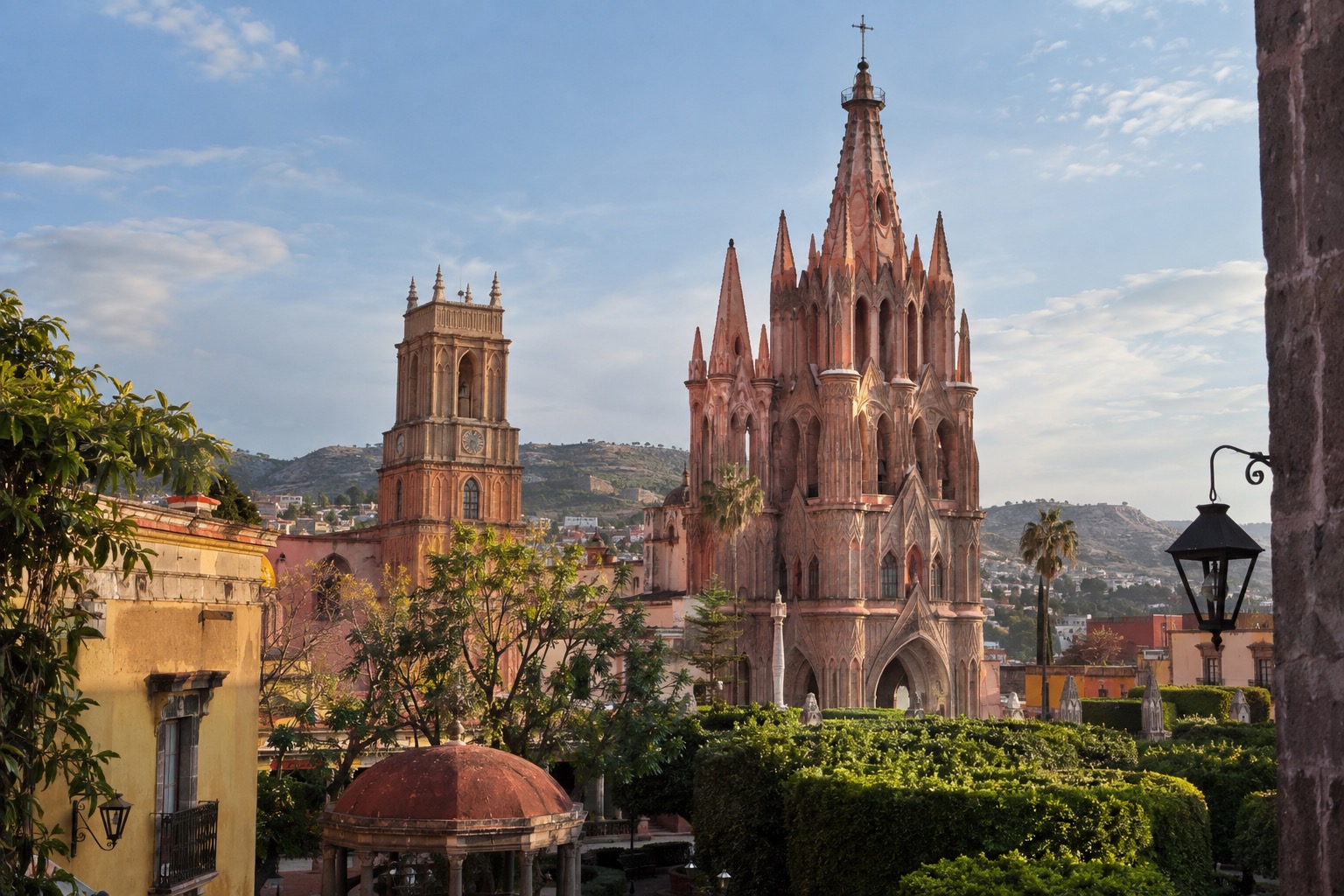 Pink neo-Gothic church towers above a plaza with trees in San Miguel de Allende