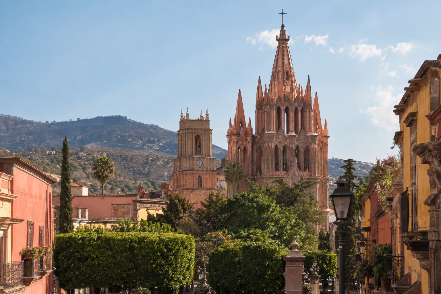 Pink neo-Gothic towers of a parish church rising above a tree-lined plaza and colonial facades