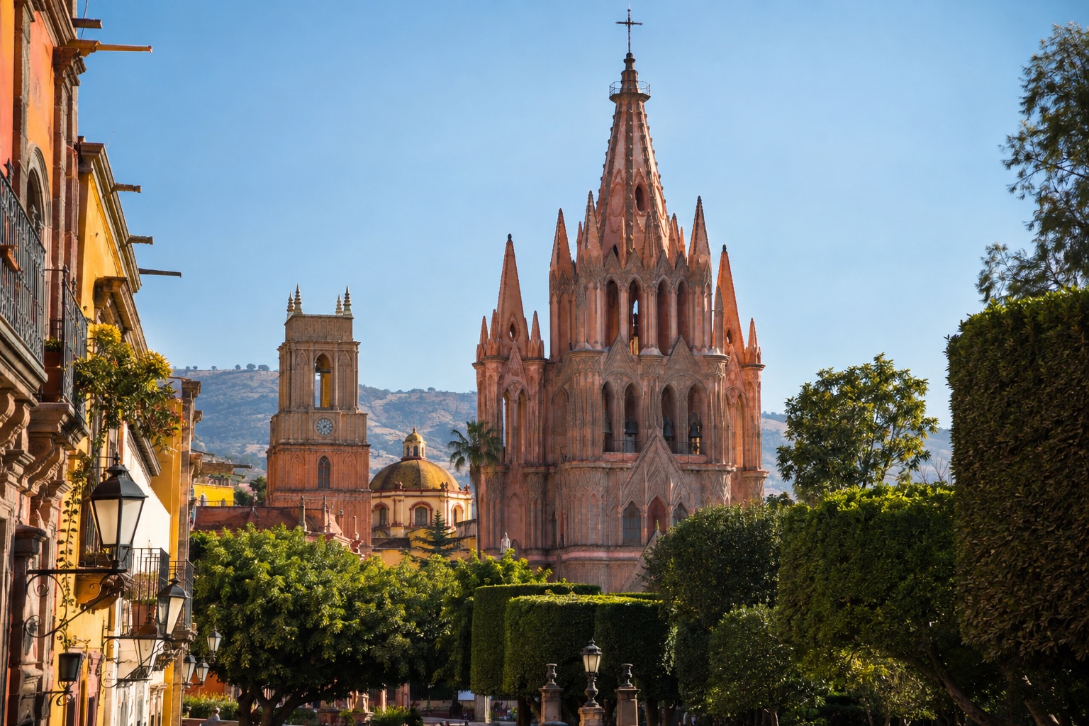 Pink neo-Gothic church towers rising above a tree-lined plaza in San Miguel de Allende