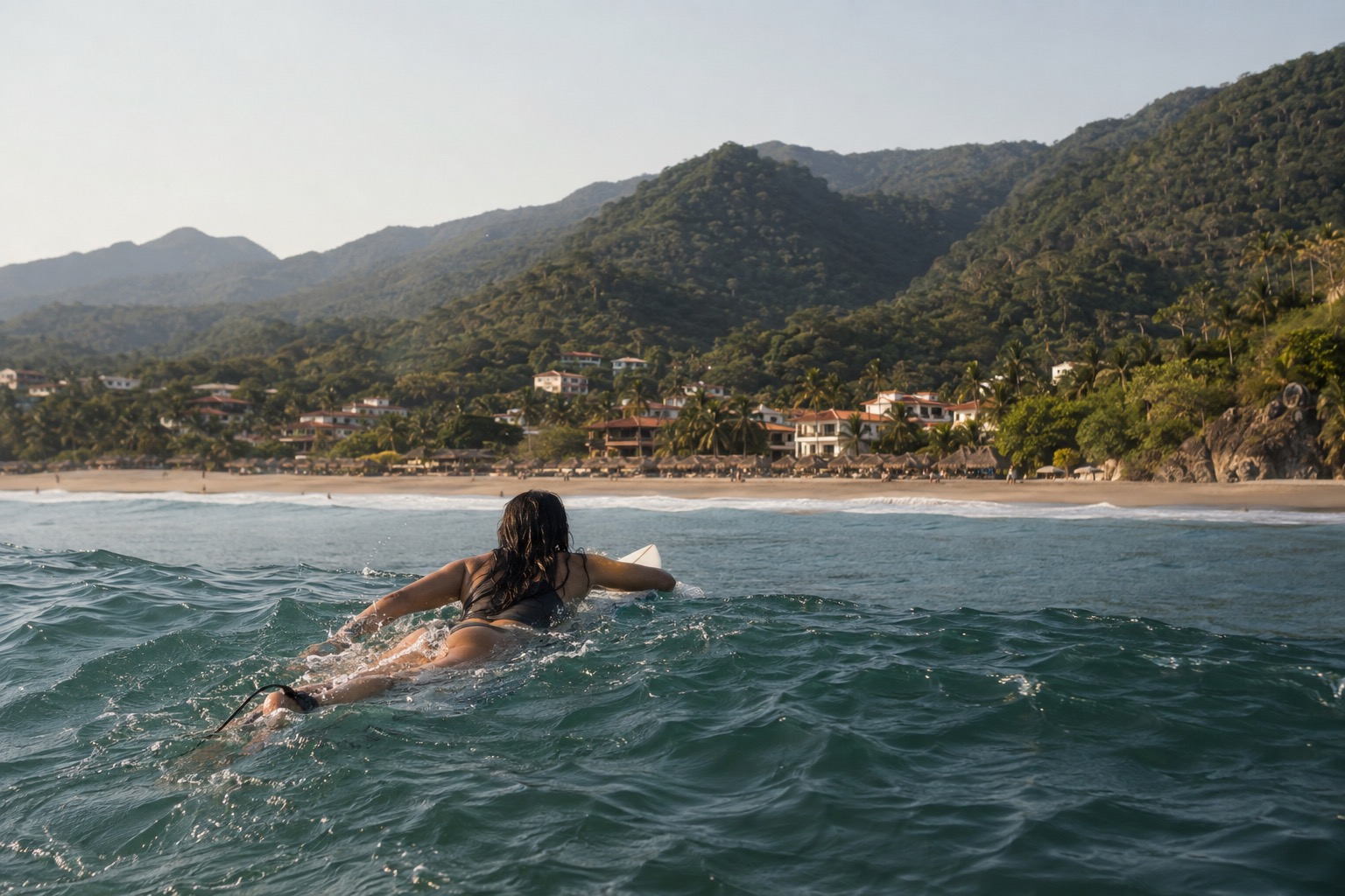 A surfer paddling out over a small wave at a sandy beach