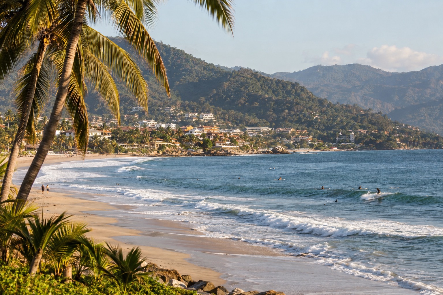 Palm-fringed beach with surfers in the water and a small town behind the sand on Mexico's Pacific coast