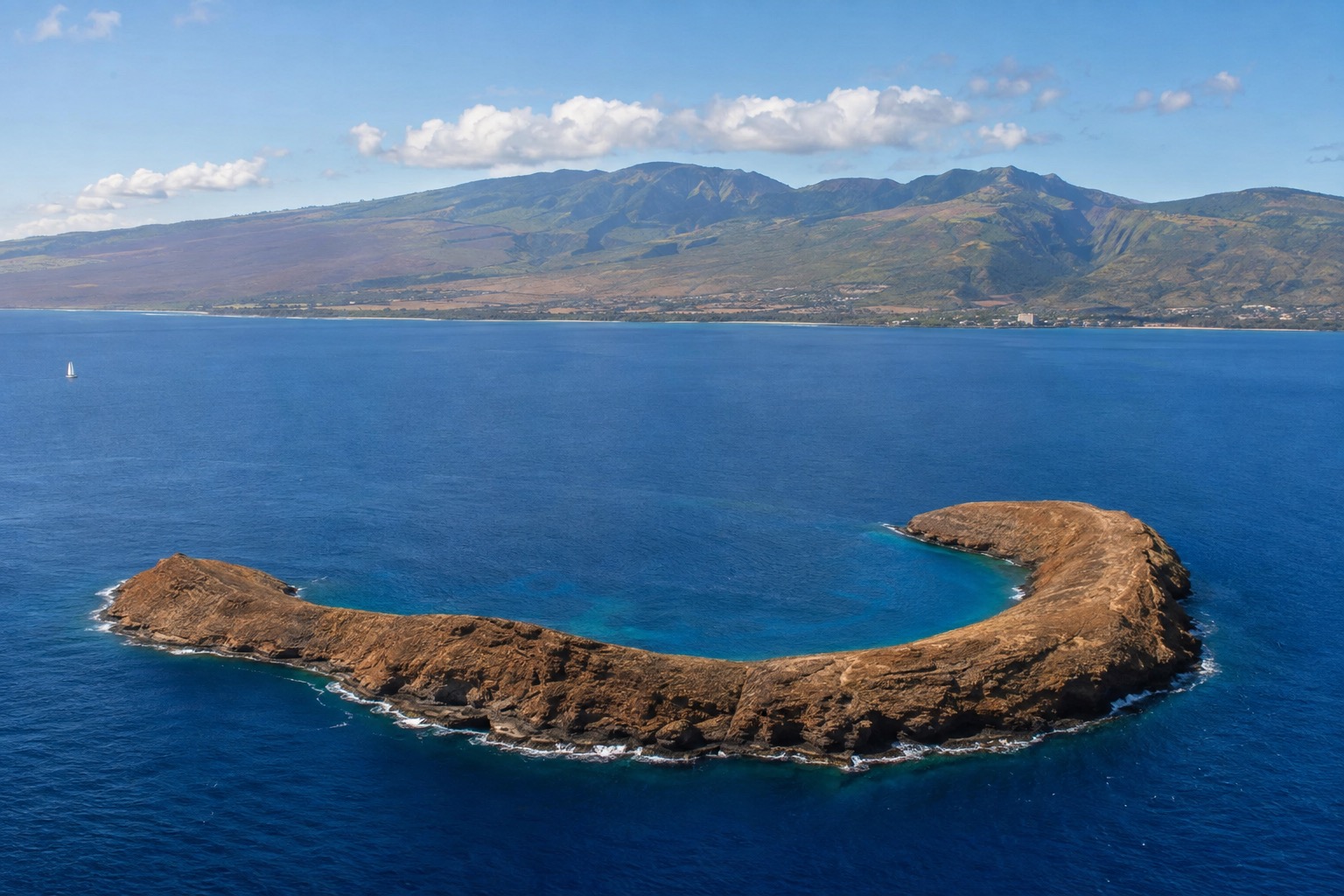 The crescent rim of Molokini crater rising from calm blue water off Maui's south coast