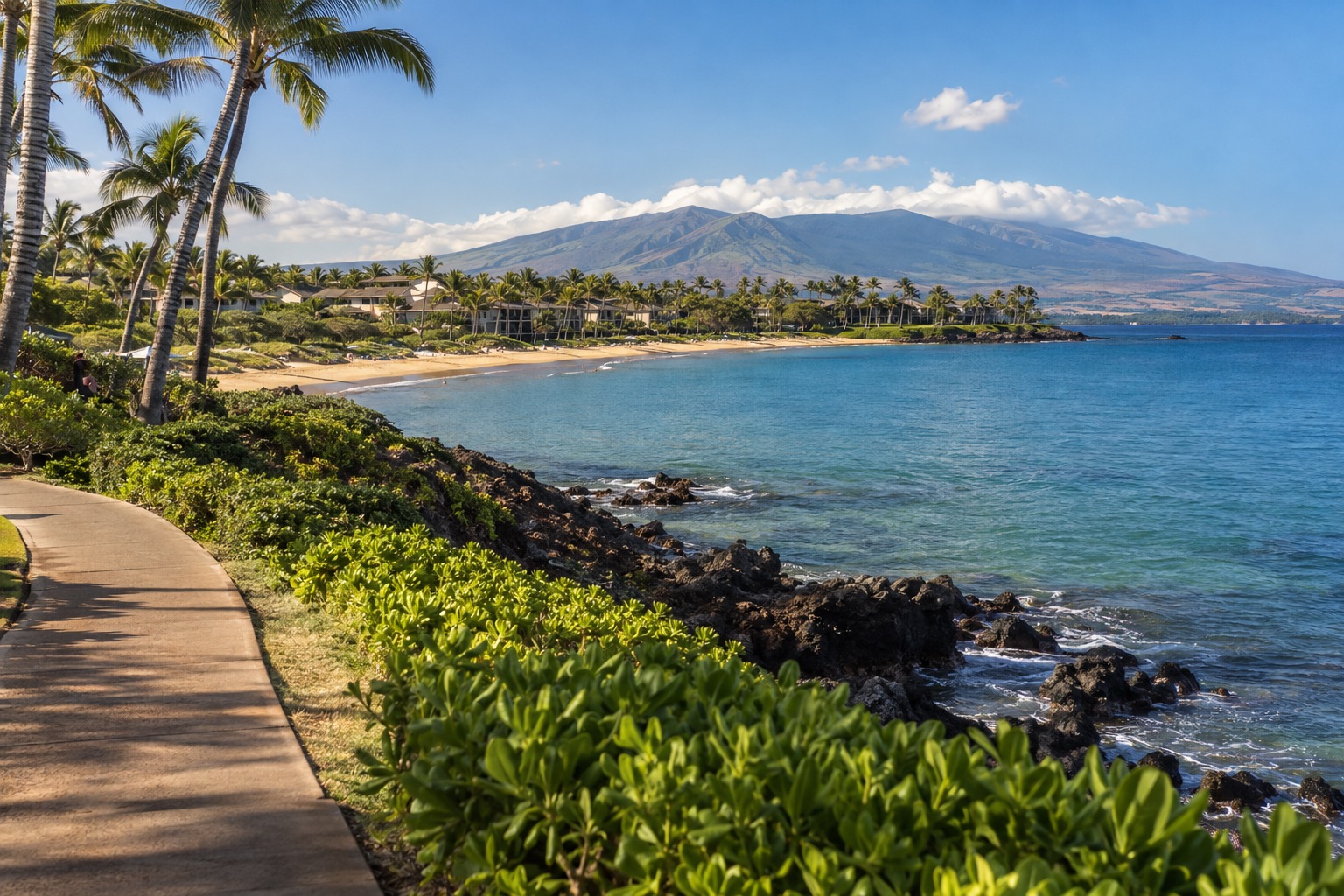 A crescent beach in Wailea with calm turquoise water and a paved coastal path in the foreground