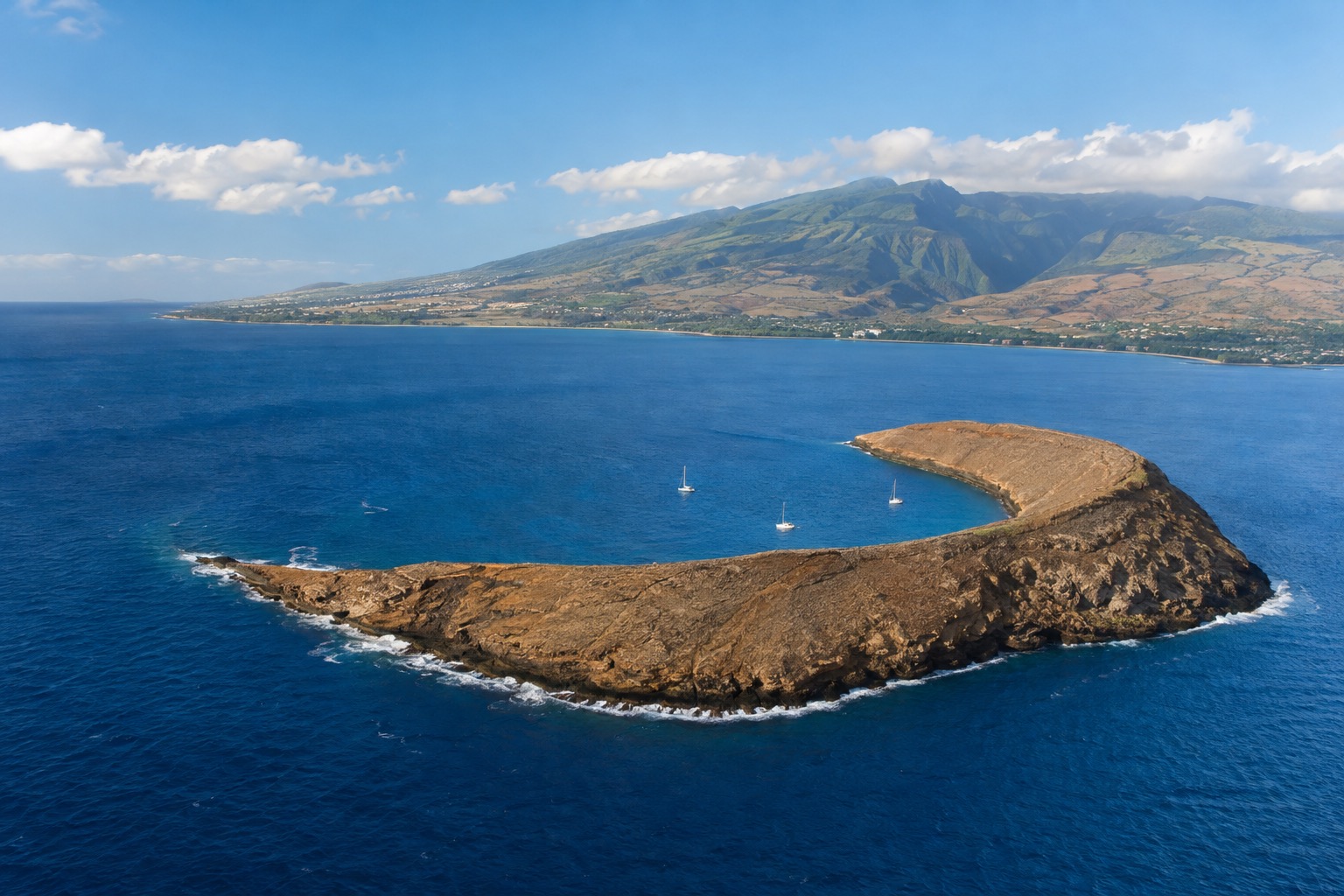 The curved rim of an extinct volcanic crater rising from the ocean off Maui's southwest coast