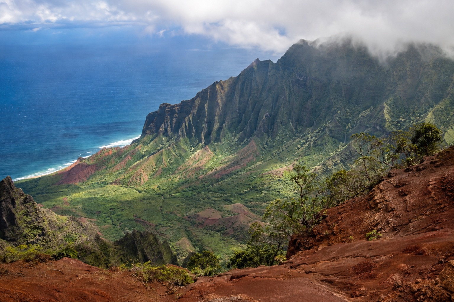 Layered red and green canyon walls beneath low cloud at a Waimea Canyon overlook