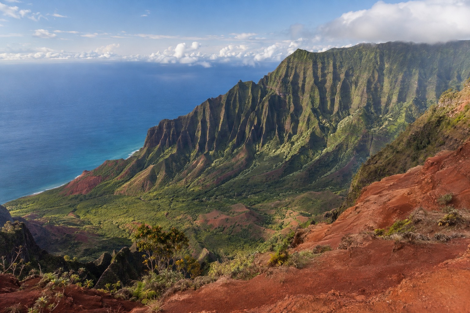 A wide red-rock gorge with layered cliffs under a partly clear sky, seen from an overlook