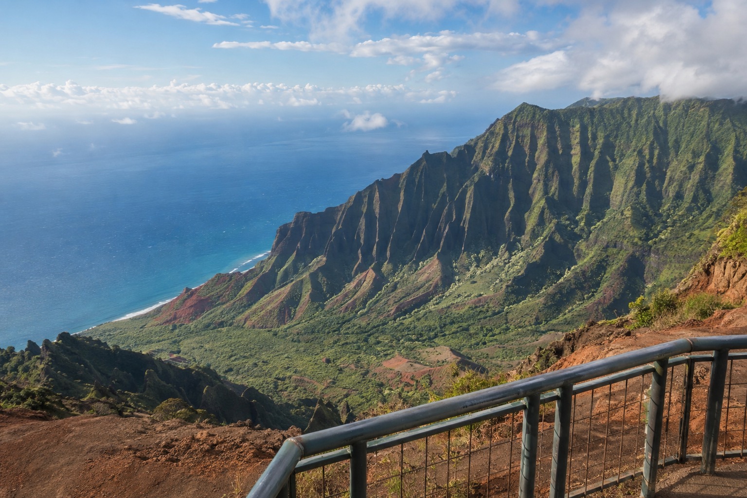 A lookout railing above layered red and green canyon walls at Kokee