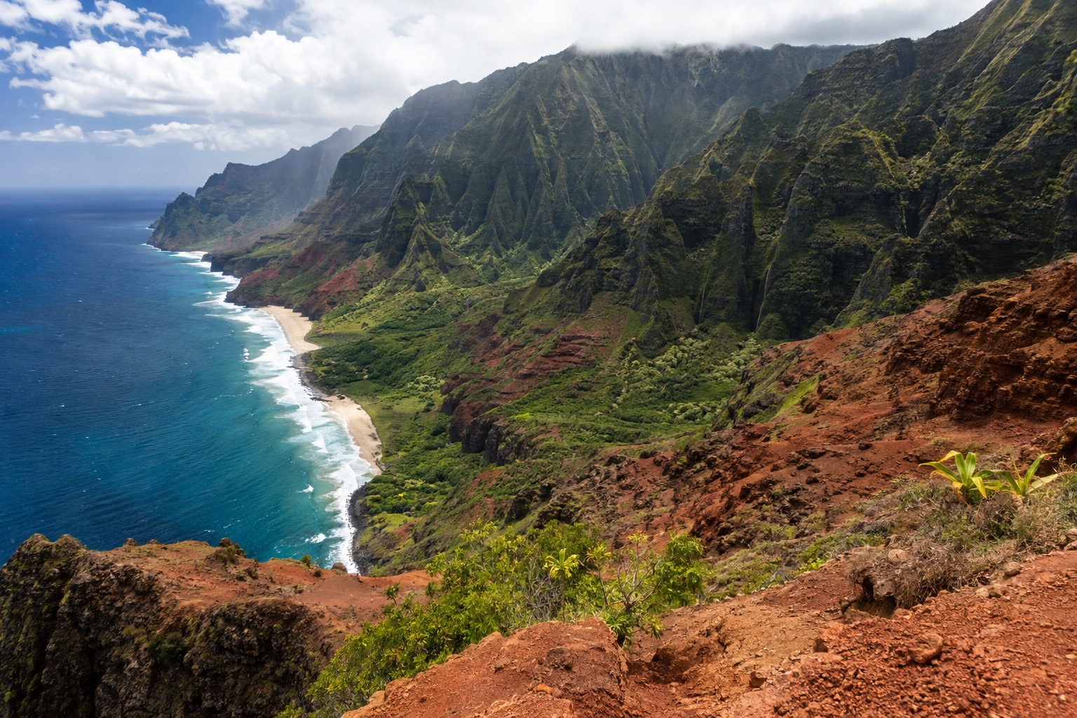 A deep red-walled canyon with layered cliffs under a partly cloudy sky