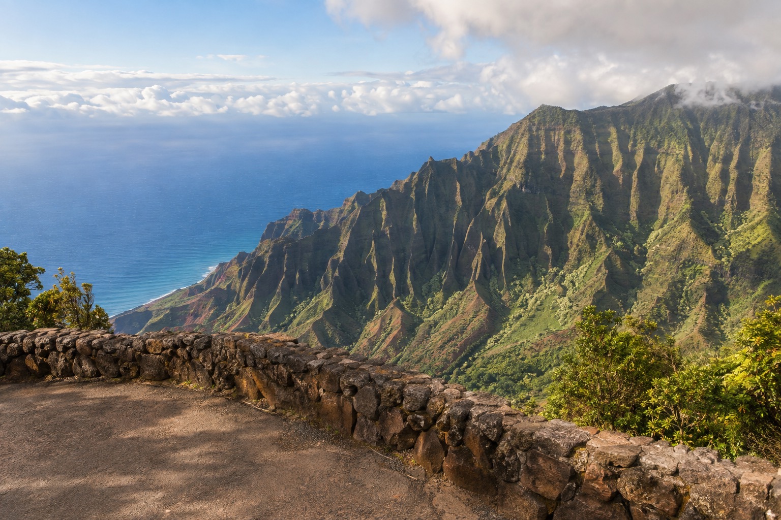 A paved overlook area with a low stone wall facing a deep canyon under morning light